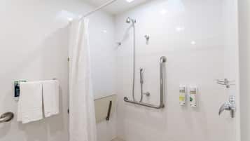 A modern bathroom with white tiles, a shower with a handheld showerhead, a grab bar, and a towel rack with two towels.