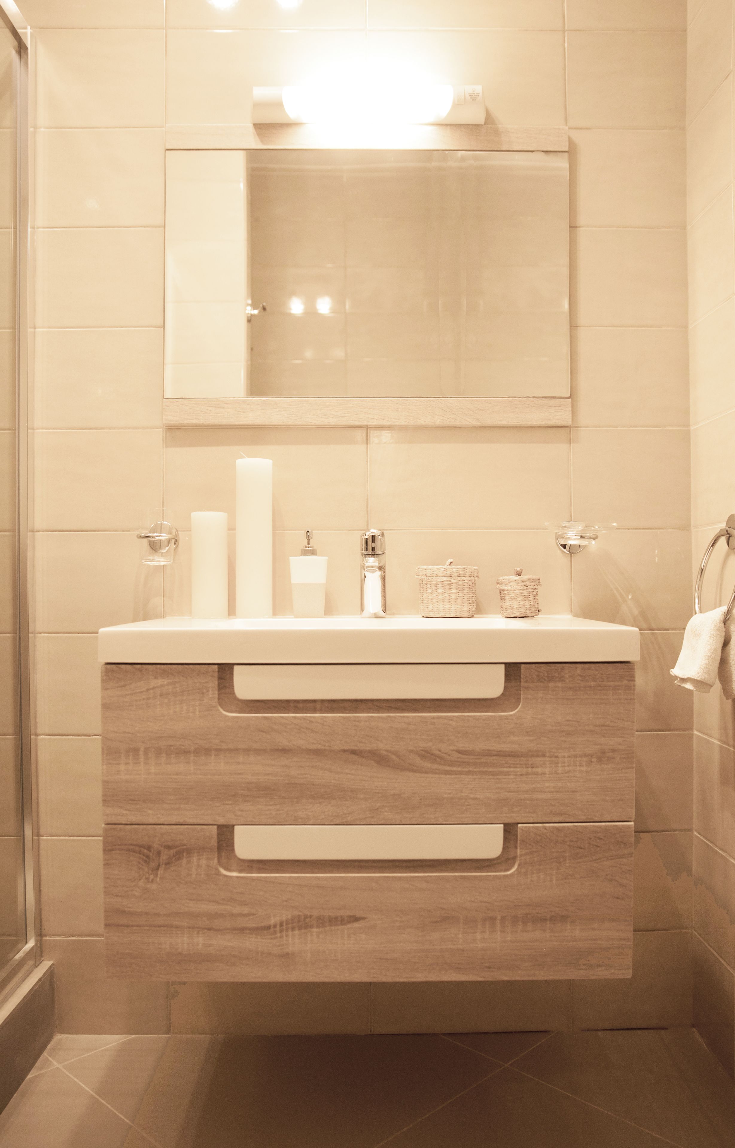 A modern bathroom with a wooden vanity, a mirror, and a toilet paper holder.