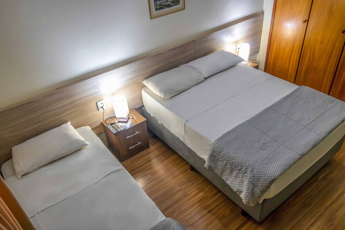 A hotel room with two beds, a wooden headboard, a bedside table with a lamp, and a wardrobe.
