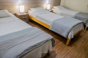 A hotel room with three single beds, wooden flooring, and bedside lamps. - Hotel Portucali (Ribeirão Preto)