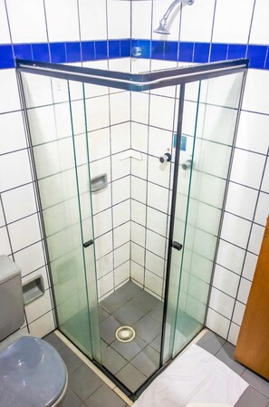 A glass-enclosed shower stall with a white tiled wall and a blue-tiled shower area. - Hotel Portucali (Ribeirão Preto)