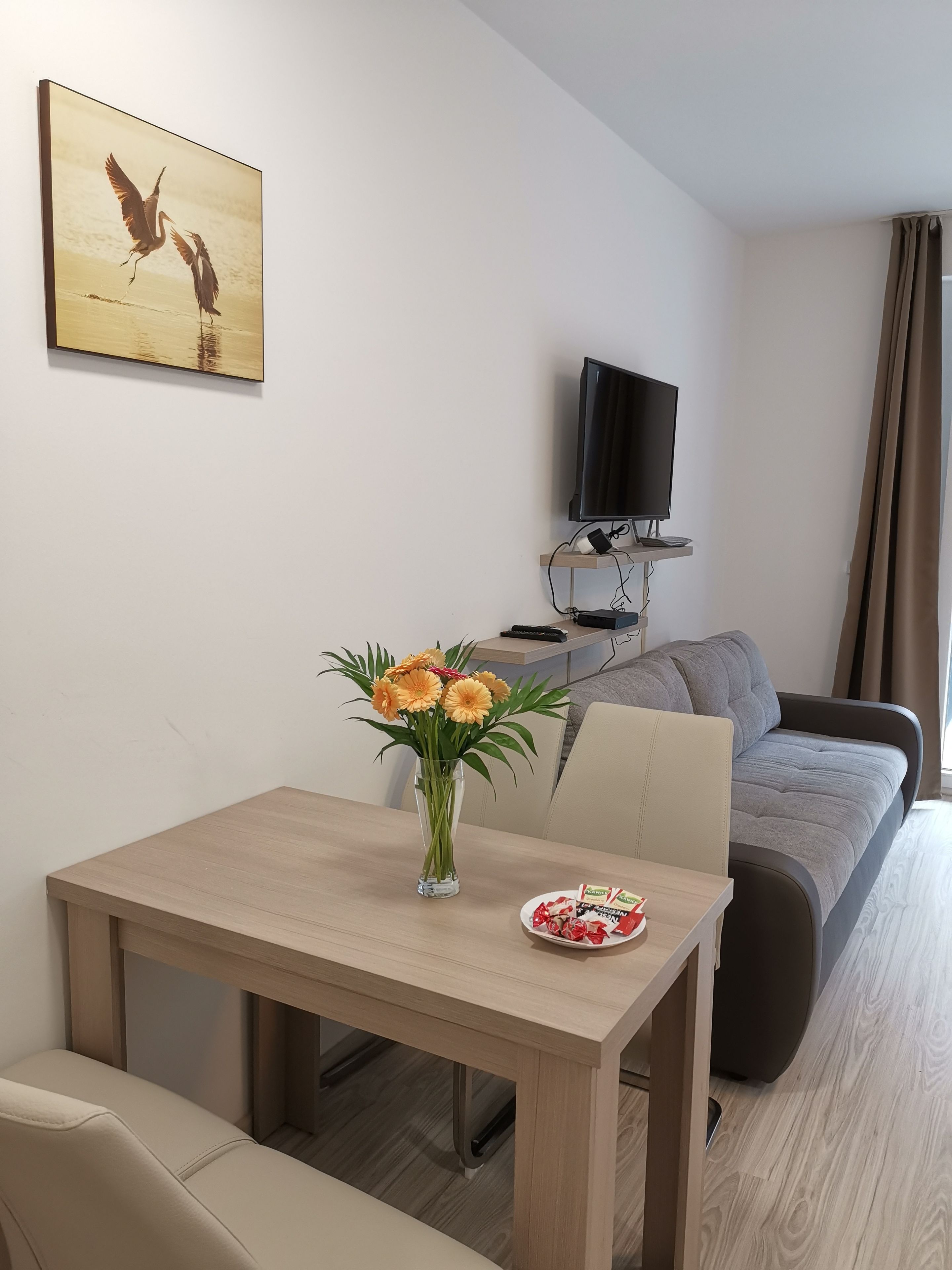 Una habitación de hotel moderna con una mesa de comedor de madera, un jarrón de flores, un televisor de pantalla plana y un sofá.