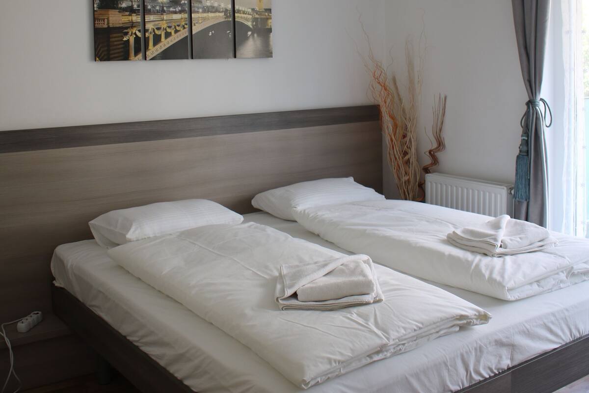 Een tweepersoonsbed met witte lakens, een hoofdbord en een stadsgezichtschilderij aan de muur.