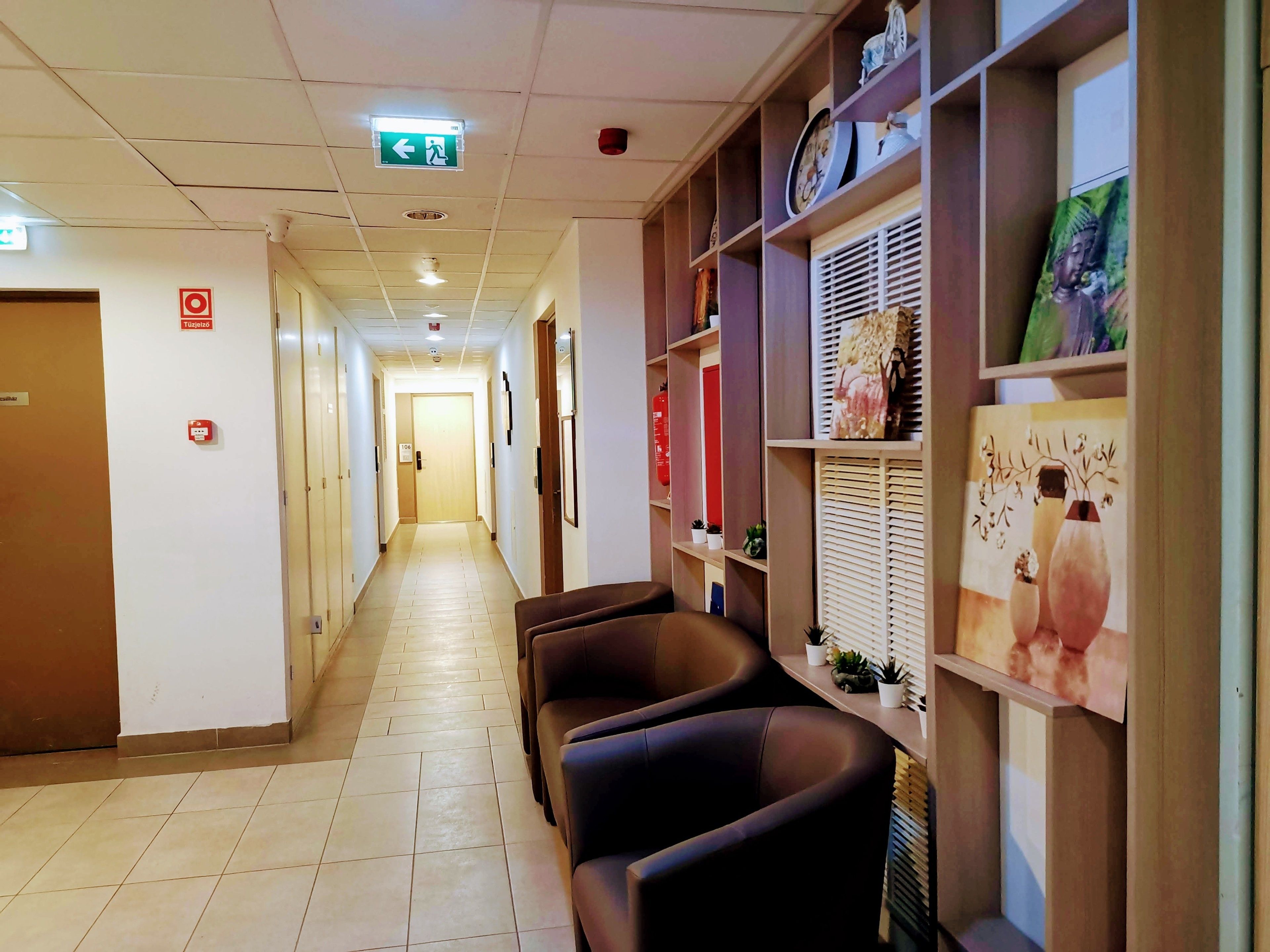 A hotel corridor with a reception desk, a fire alarm, and a sign indicating the exit direction.