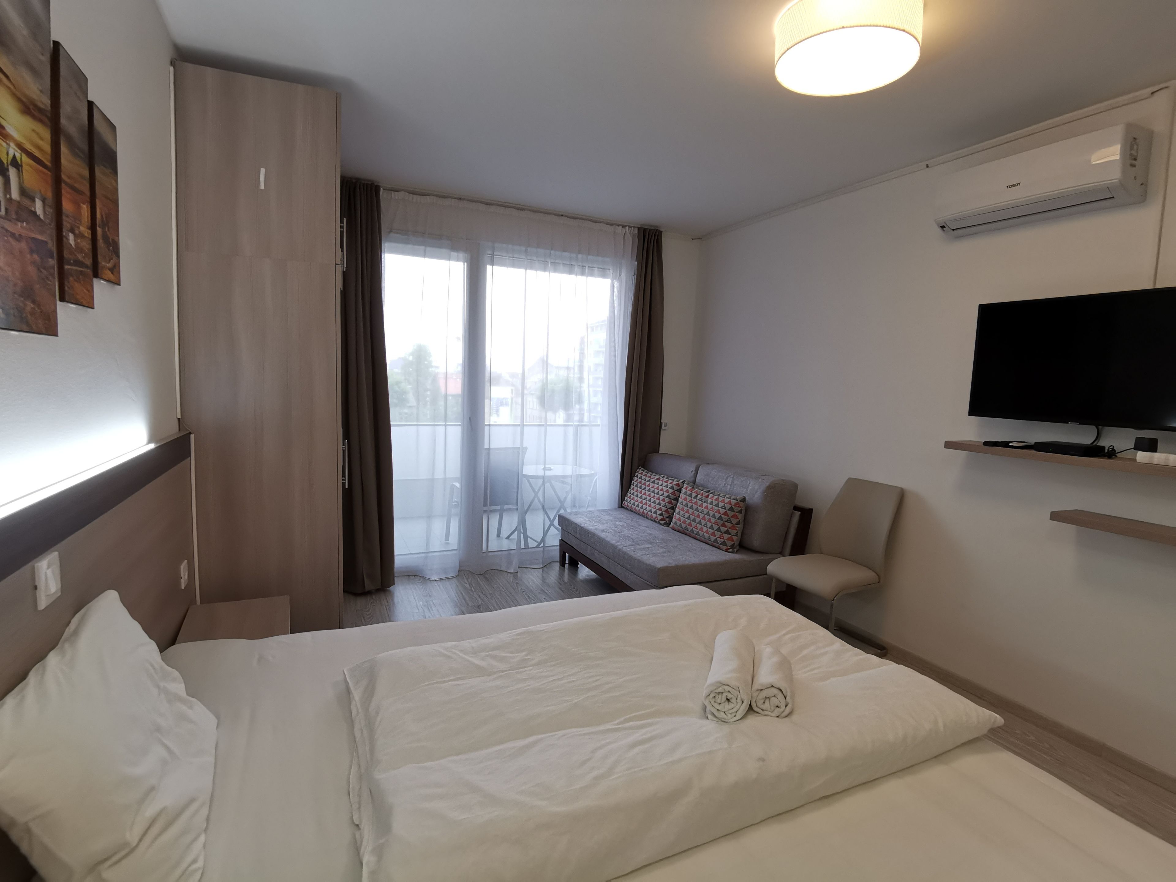 A hotel room with a bed, a sofa, a TV, and a balcony with curtains.
