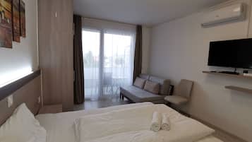 A hotel room with a bed, a sofa, a TV, and a balcony with curtains.