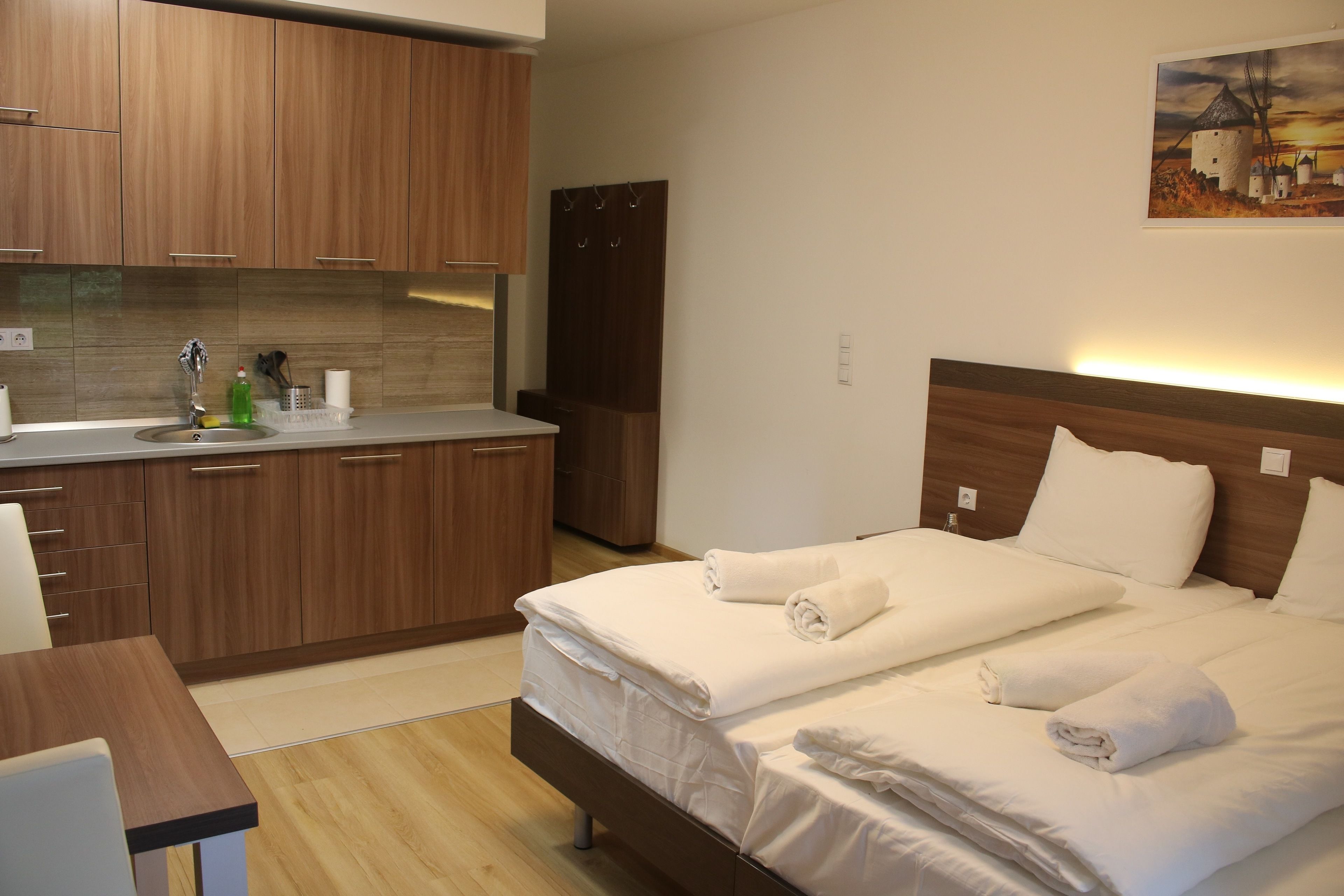 A hotel room with a wooden bed, a wooden desk, and a kitchenette with a sink and cabinets.