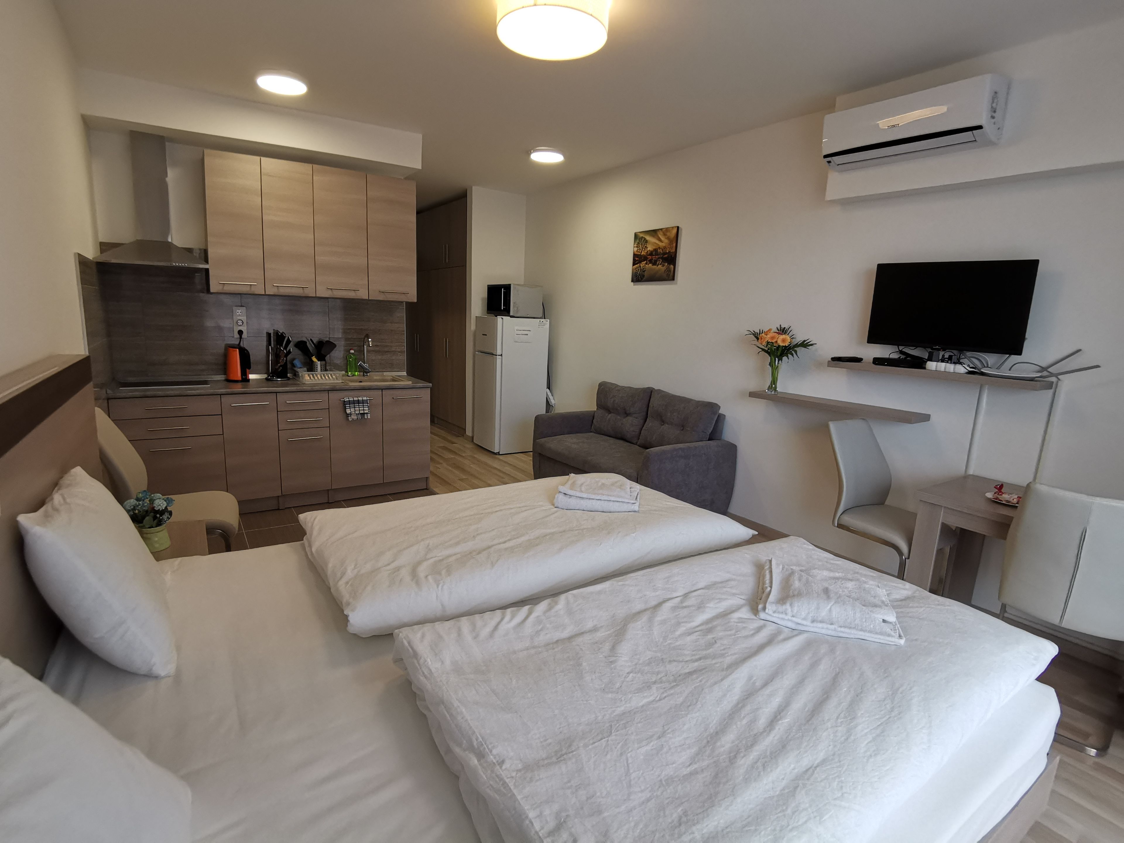 A hotel room with two beds, a kitchenette, a flat-screen TV, and a small table.