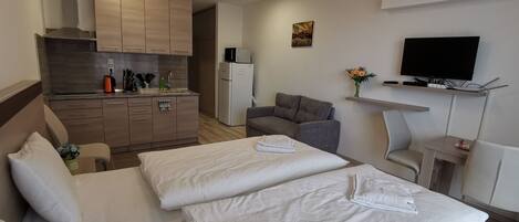 A hotel room with two beds, a kitchenette, a flat-screen TV, and a small table.