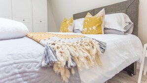 A neatly made bed with a white and yellow blanket, a grey headboard, and matching pillows. - The Manor Suite (Oxford)