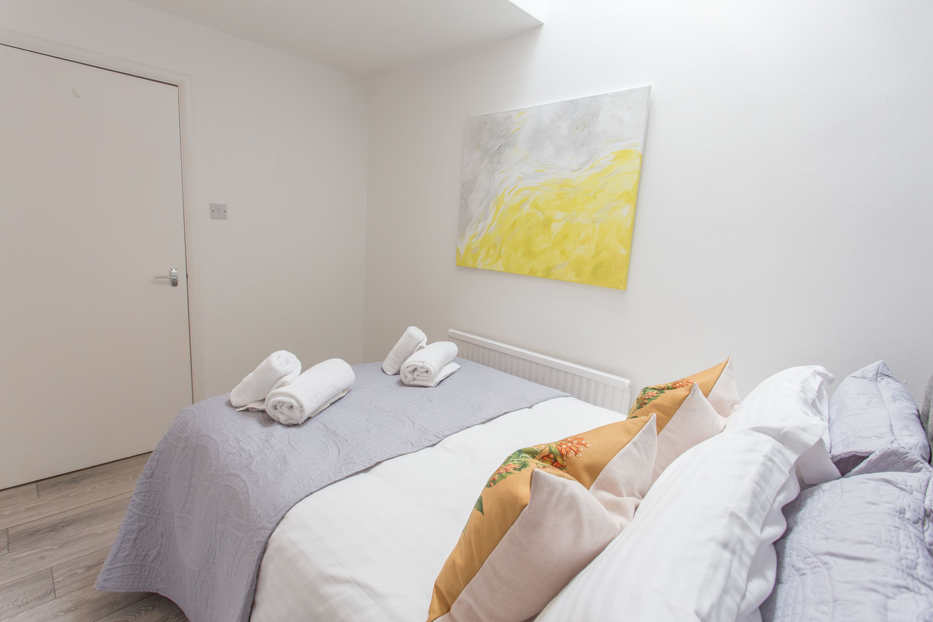 A hotel room with a bed, towels, a painting, and a door.