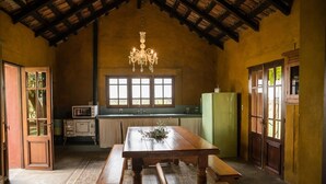 A rustic kitchen with a wooden table and bench, a chandelier, and a green refrigerator.