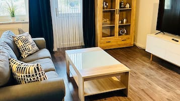 Ett modernt vardagsrum med en grå soffa, ett träskåp med glasdörrar, ett vitt TV-bord och ett träbord som används som soffbord.