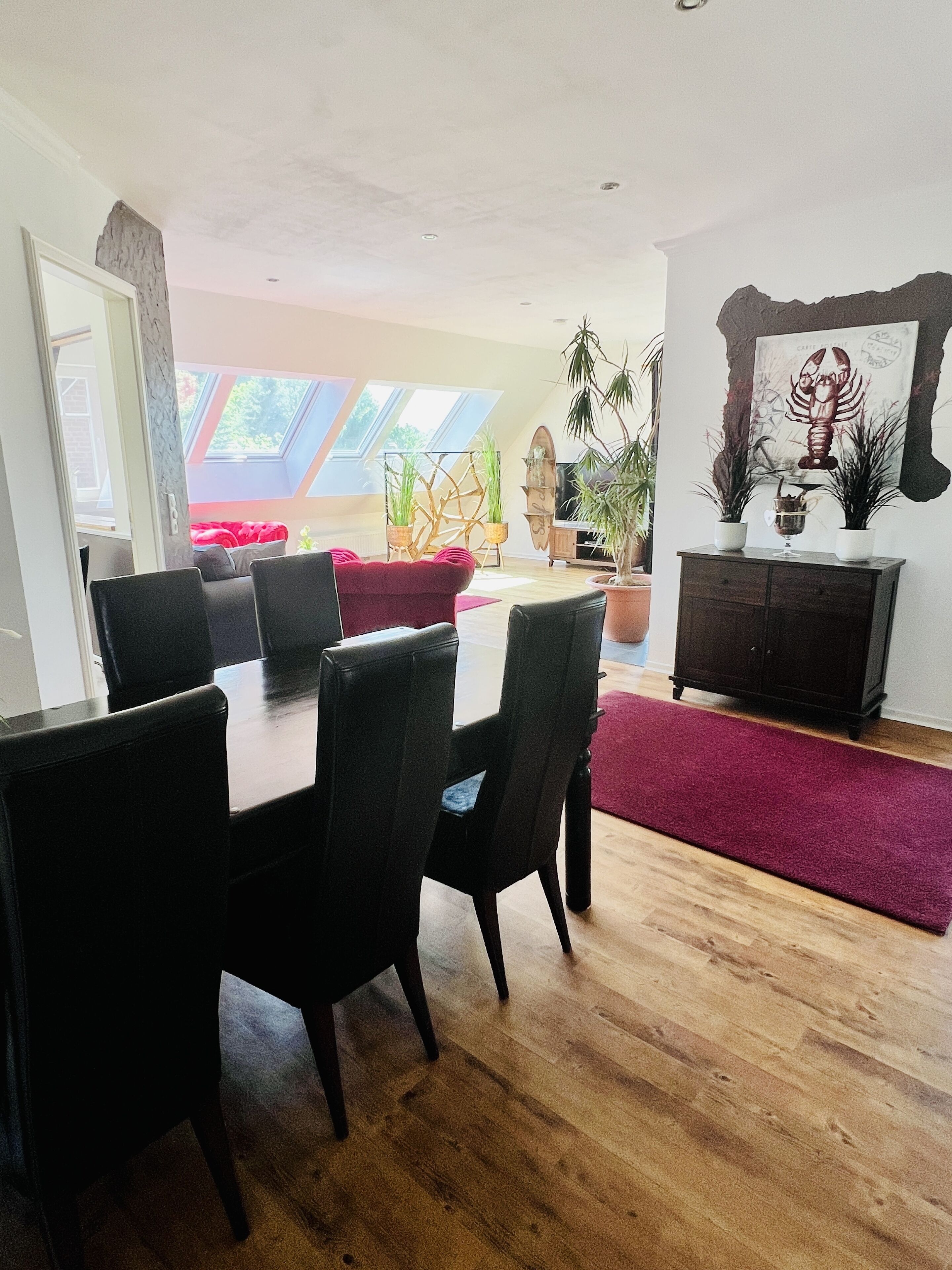 A dining area with a wooden table and chairs, a red sofa, and a TV against the wall.