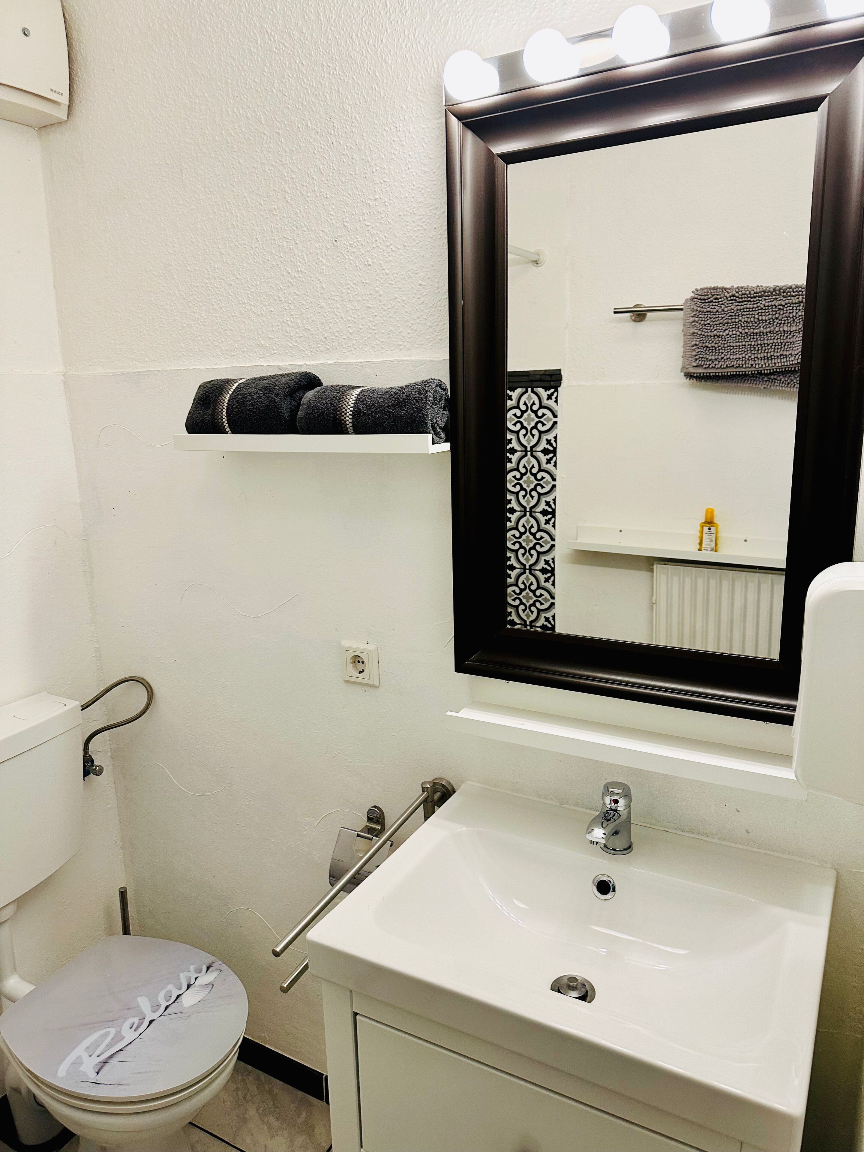 Um banheiro com pia branca, espelho iluminado, porta-toalhas e vaso sanitário.