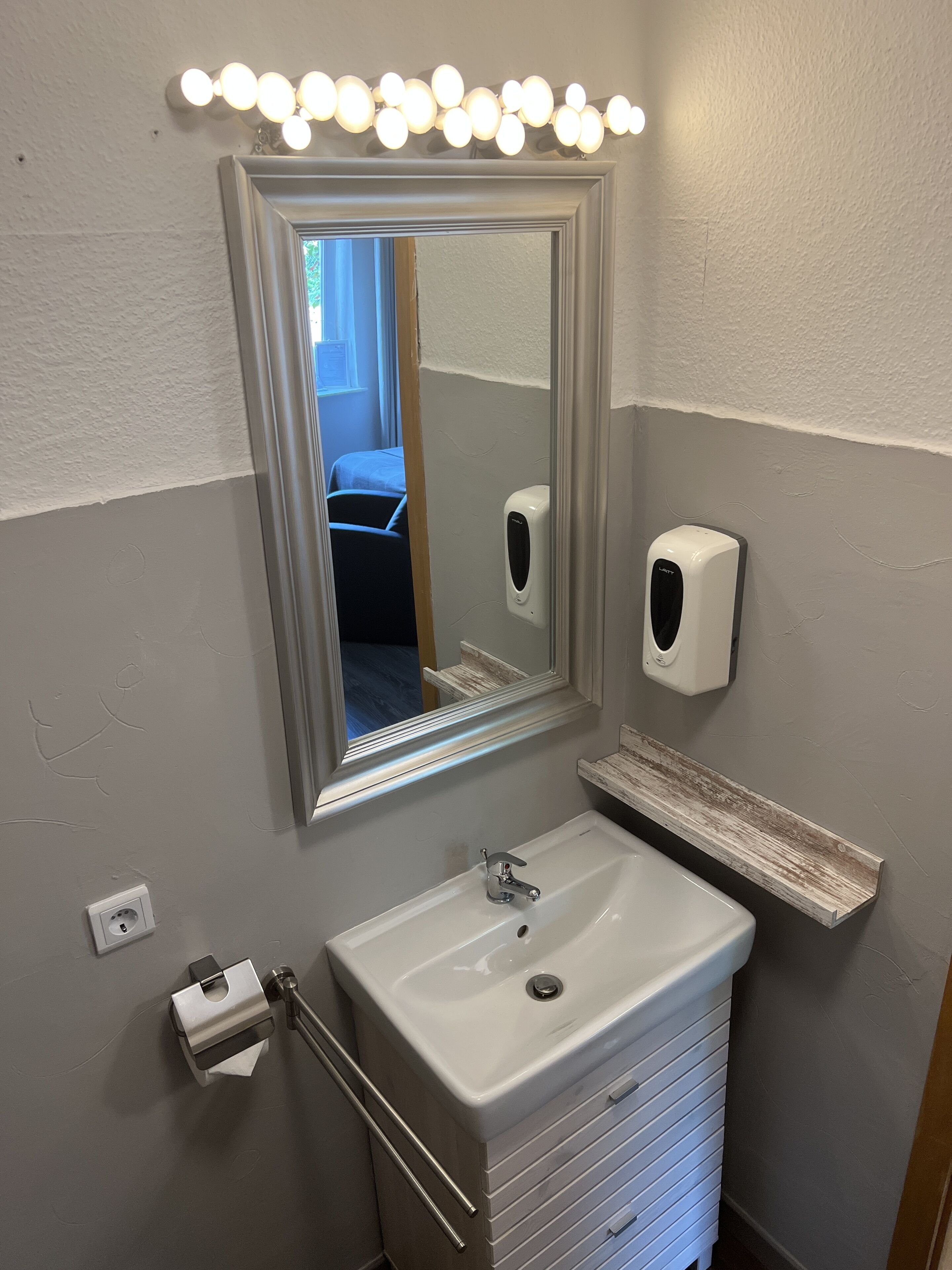 A bathroom with a vanity, a mirror, a soap dispenser, and a towel dispenser.
