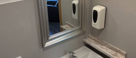 A bathroom with a vanity, a mirror, a soap dispenser, and a towel dispenser.
