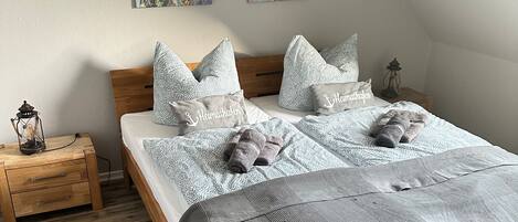 Un dormitorio con cama de madera, ropa de cama gris y dos cuadros en la pared.