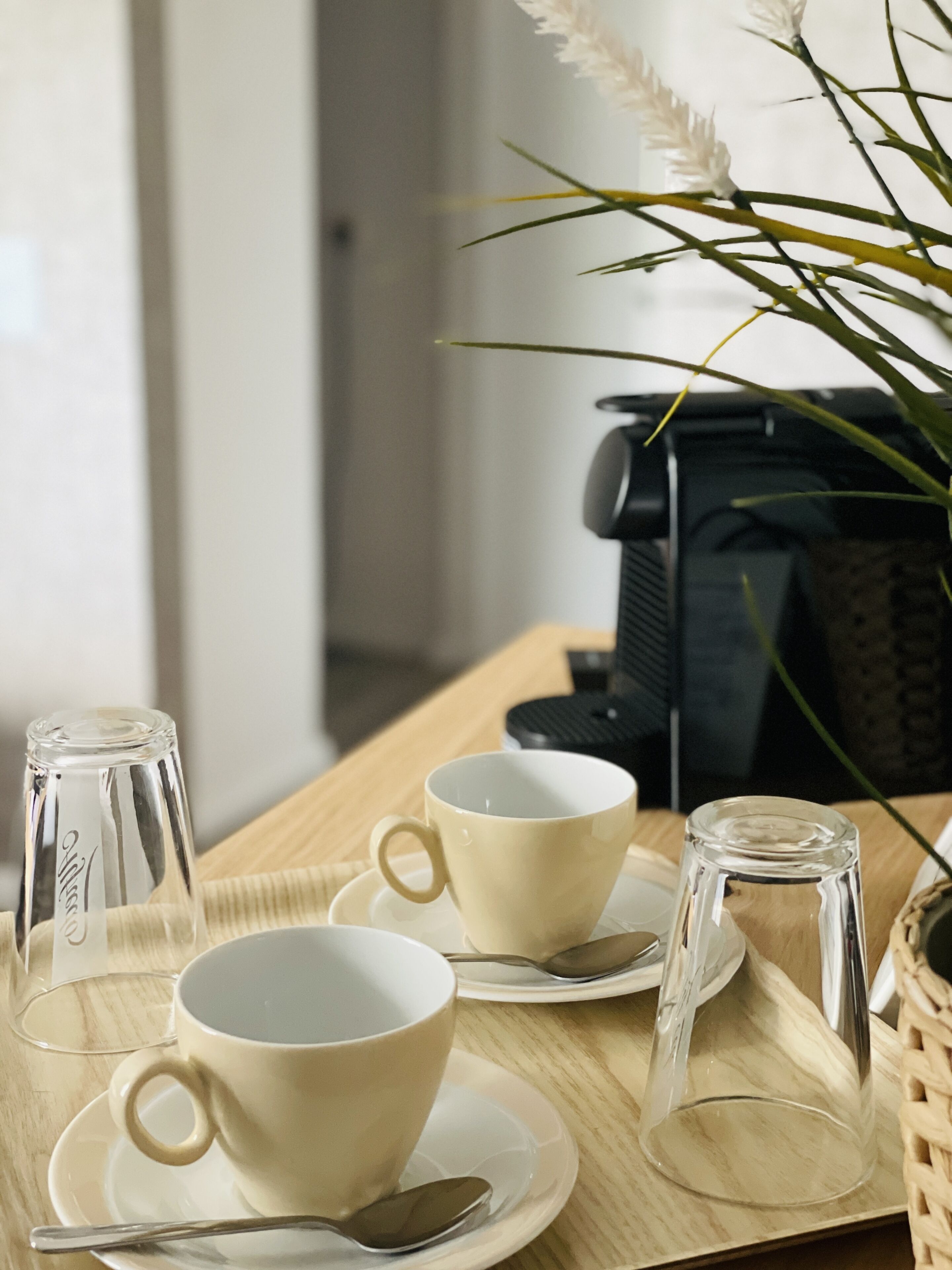 A table with two white cups, a glass, and a spoon on a wooden table.