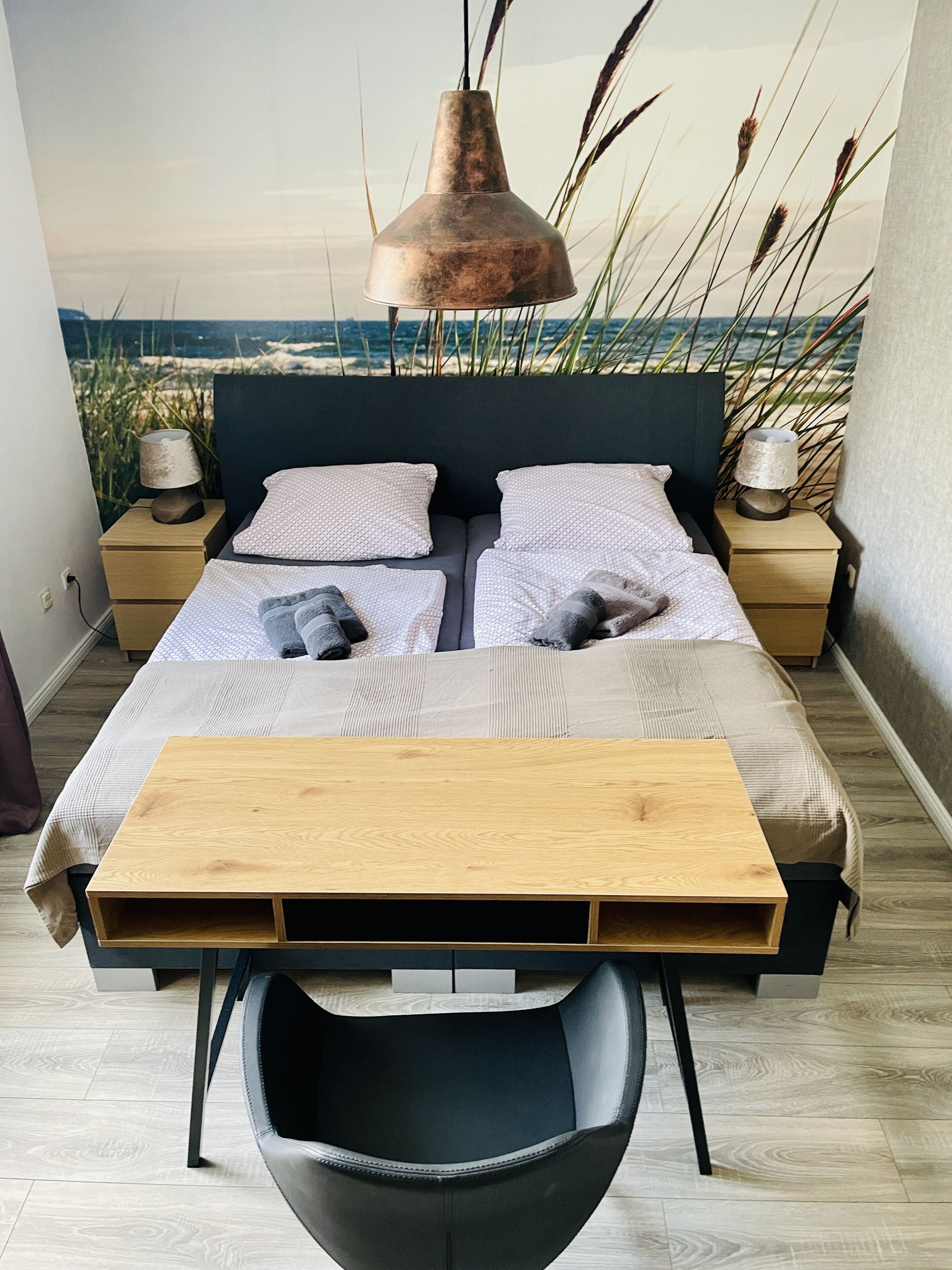 A modern bedroom with a bed, bedside tables, a wooden desk, and a chair.