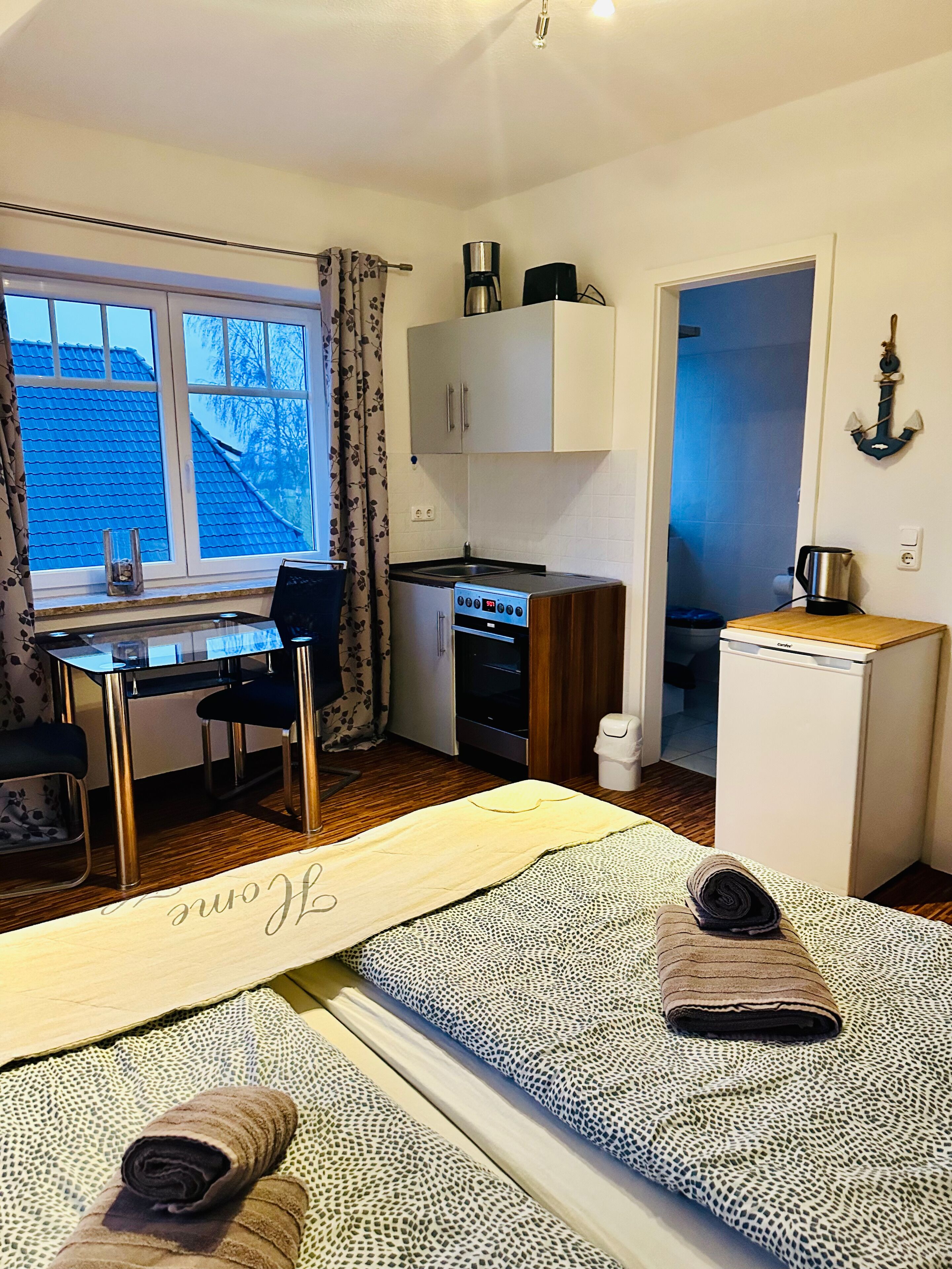 Et lille værelse med tekøkken, en seng med dekorativt sengegavl, et lille bord og en stol.