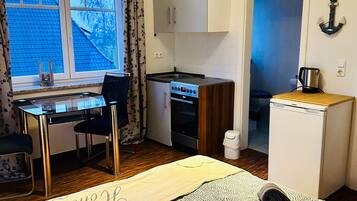 A compact room with a kitchenette, a bed with a decorative headboard, a small table, and a chair.