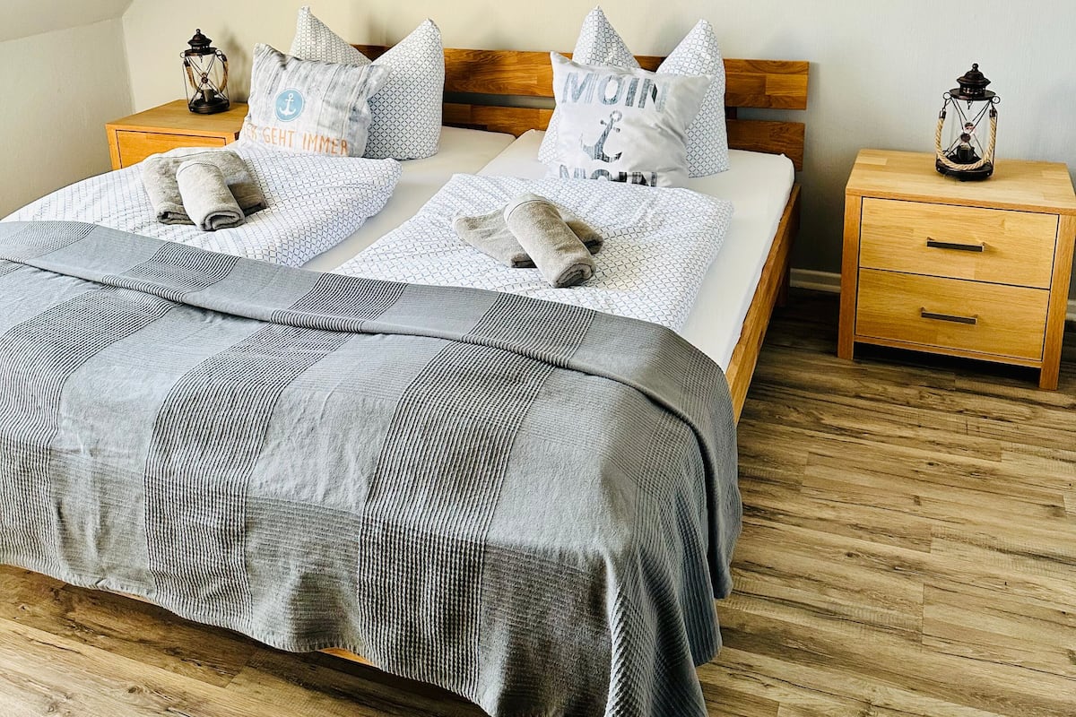 A bedroom with a bed, a nightstand, a wall-mounted lamp, and a painting of a boat on water.