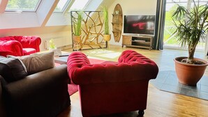 A modern living room with a red sofa, a brown sofa, and a wooden coffee table. There is a TV, a potted plant, and a decorative wall piece. - Haus Stern (Wangels)