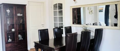 A dining area with a wooden table and chairs, a dark wooden cabinet, and a large mirror on the wall.