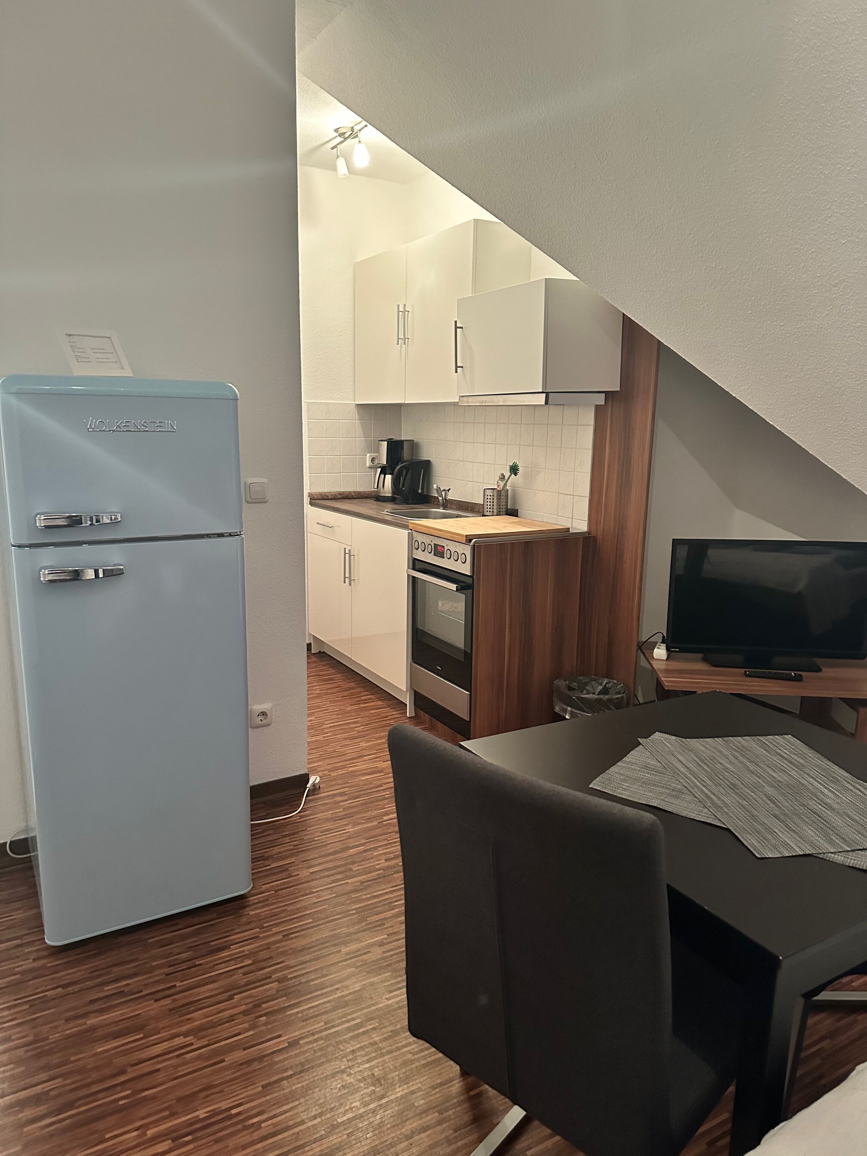 Eine kleine Küche mit einem hellblauen Kühlschrank, einem Herd, einem Waschbecken und einem Fernseher auf einem Holztisch.