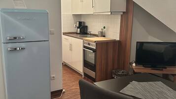 Een kleine keuken met een lichtblauwe koelkast, een fornuis, een spoelbak en een televisie op een houten tafel.