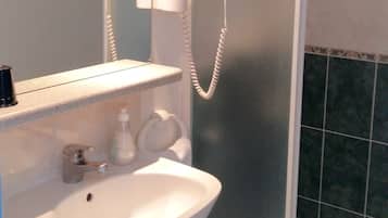 Un baño con lavamanos blanco, espejo y zona de ducha con puerta de cristal.