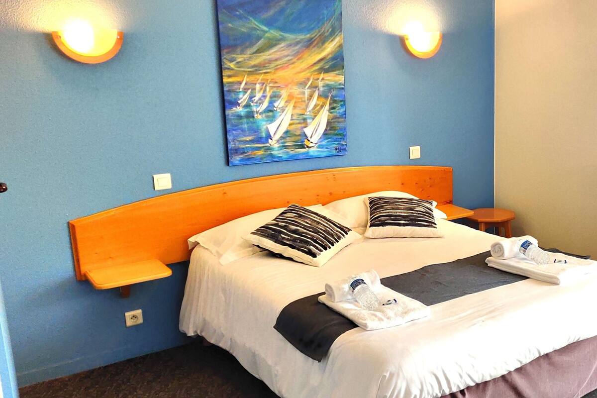 A hotel room with a bed, pillows, a painting on the wall, and a radiator.