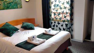 Une chambre d’hôtel avec un lit, des oreillers verts, une fenêtre avec des rideaux à motifs de papillons et un tableau au mur.