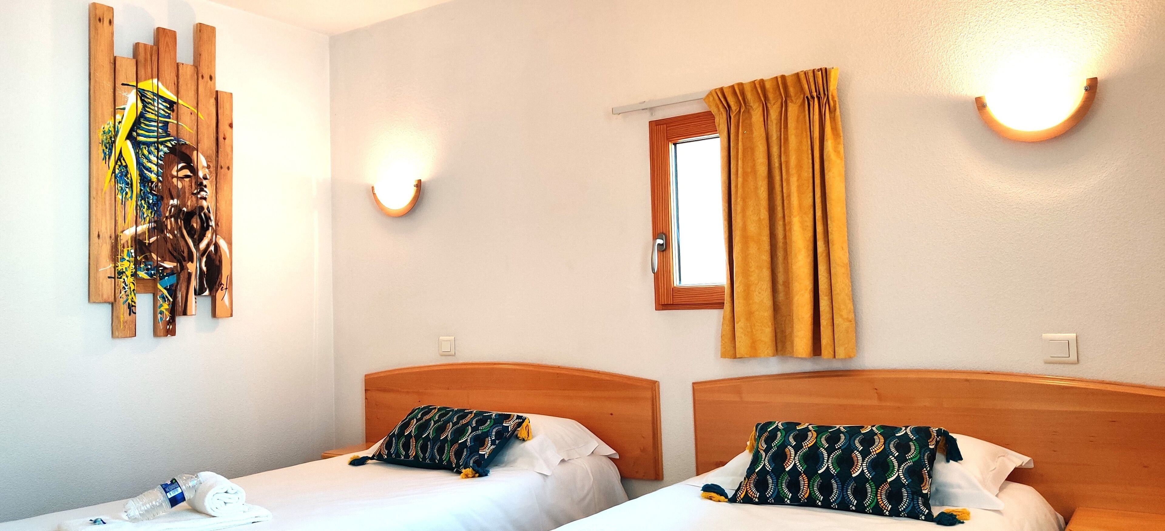 Habitación de hotel con dos camas, cabecera de madera, una obra de arte en la pared, ventana con cortinas y una lámpara de pared.