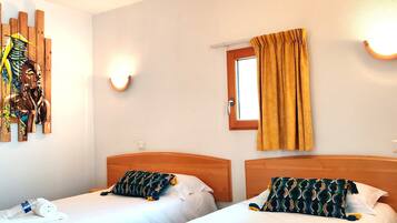 Habitación de hotel con dos camas, cabecera de madera, una obra de arte en la pared, ventana con cortinas y una lámpara de pared.