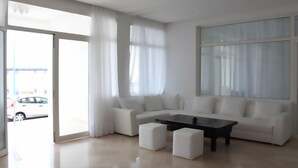 Una sala moderna con un sofá seccional blanco, una mesa de centro negra y un ventanal con cortinas translúcidas.