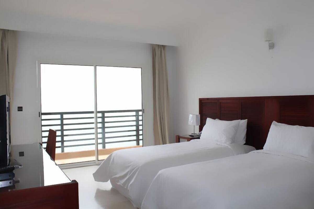 Habitación de hotel con dos camas, un escritorio, una silla, un televisor y un balcón con barandilla.