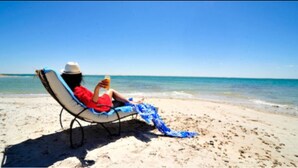 Una persona descansando en una silla de playa con una bebida, con vista al océano.