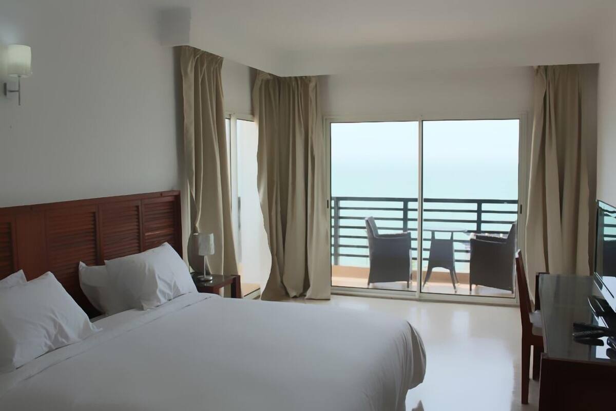 Habitación de hotel con una cama grande, un escritorio con silla y un balcón con vista al mar.
