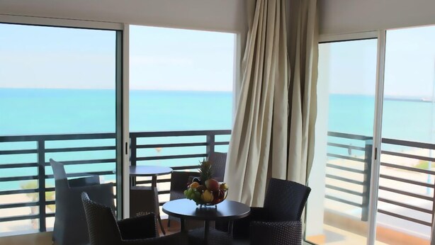Un balcón con vista al mar, una mesa con fruta y sillas de mimbre.