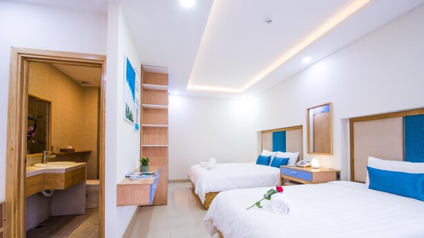A hotel room with two beds, a bathroom, a wooden shelf, and a small desk.