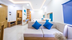 A modern hotel room with a sofa, a wooden cabinet, a bathroom, and a ceiling fan.