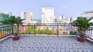 A balcony with potted plants, a tiled floor, and a cityscape view including the Avatar Hotel.