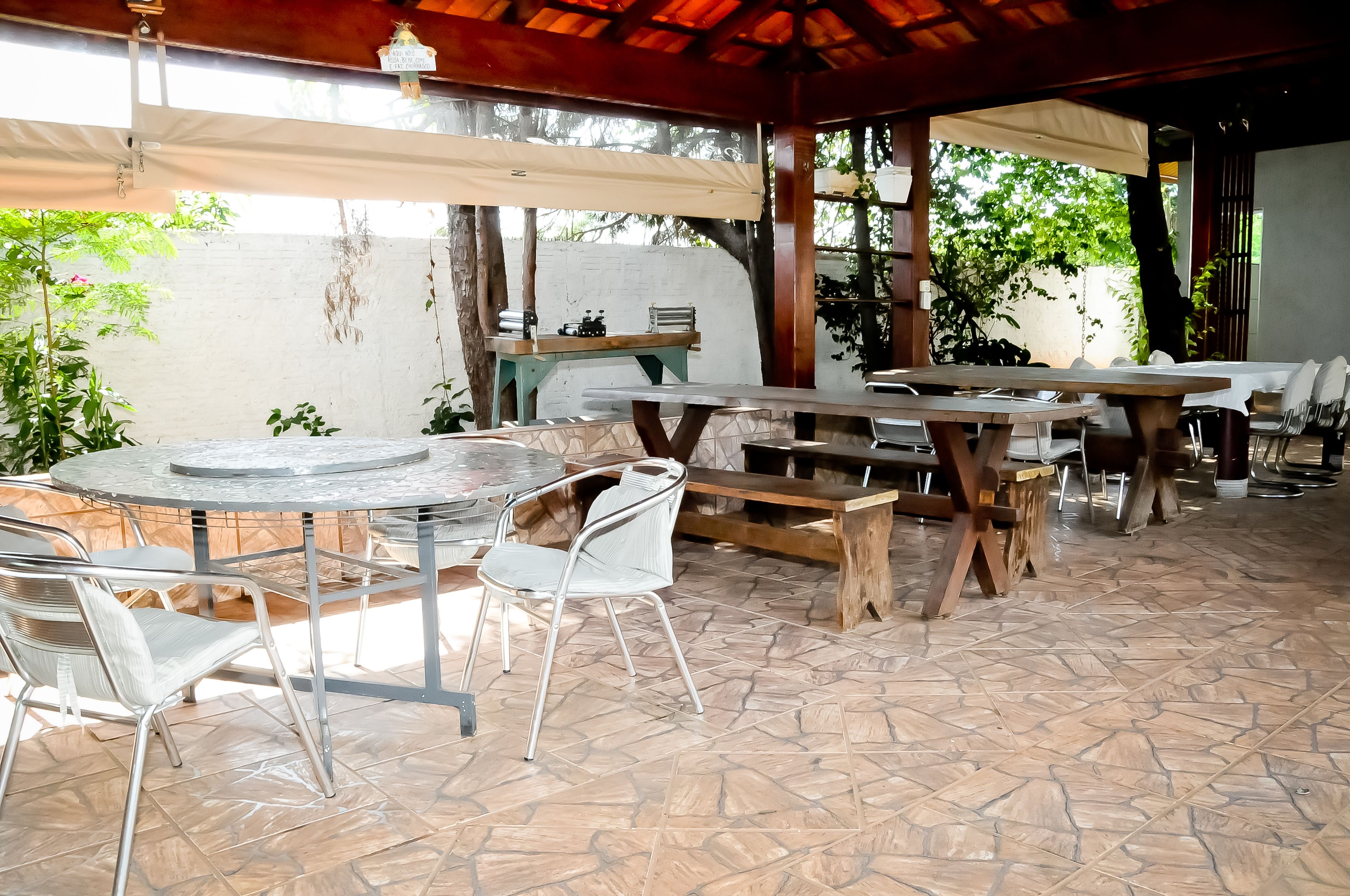 Un espacio de patio al aire libre con mesas y sillas redondas, bancos de madera y piso de baldosas.