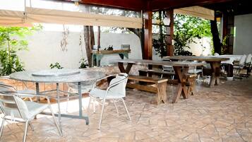 Un espacio de patio al aire libre con mesas y sillas redondas, bancos de madera y piso de baldosas.