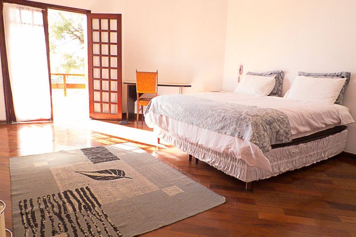 A bedroom with a bed, a chair, a wooden floor, and a view through a door.