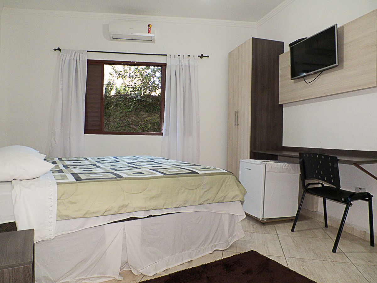 Un dormitorio con cama, escritorio, silla, televisor y ventana con cortinas.
