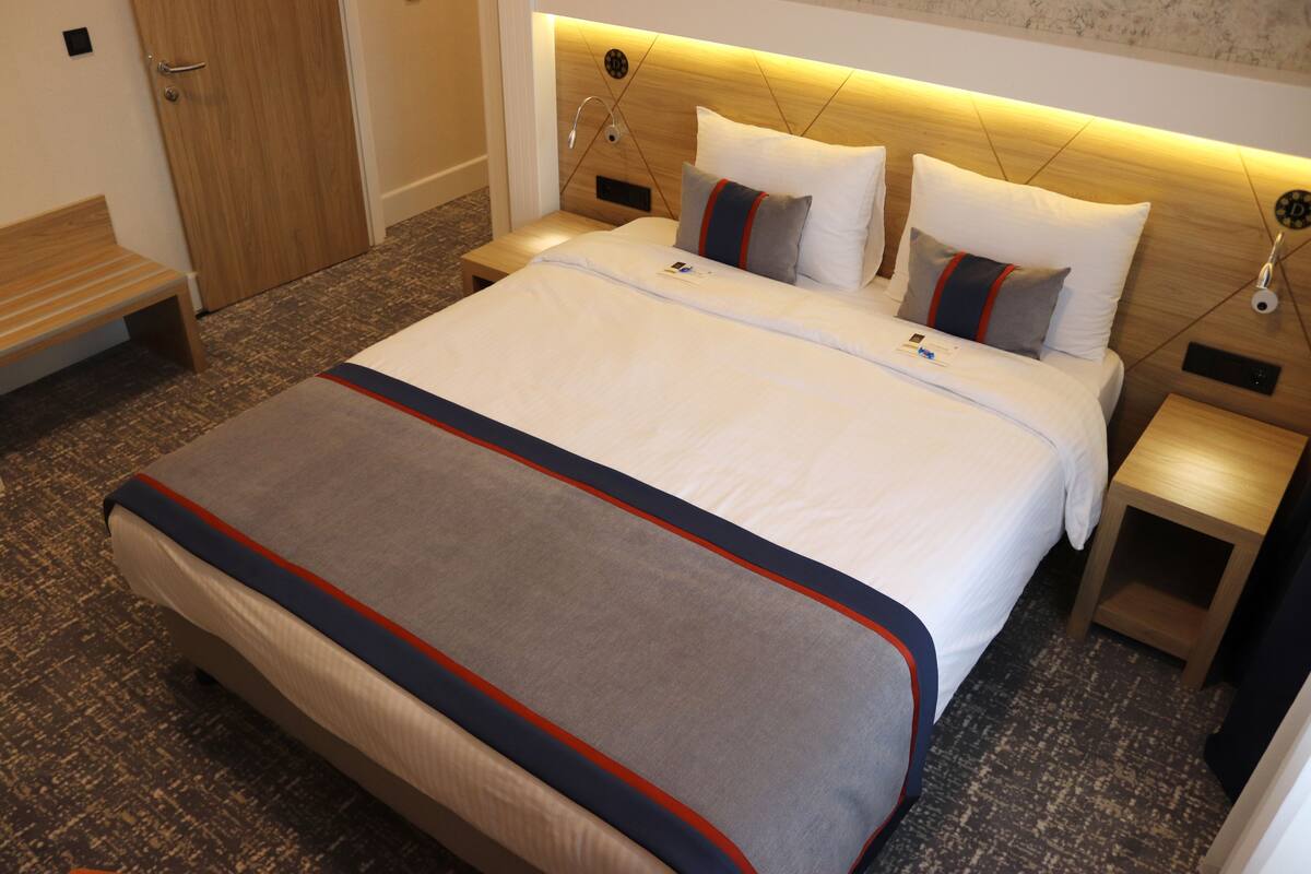 A hotel room with a large bed, a wooden headboard, a bedside table, and a bench.