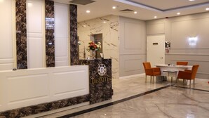Zona de recepción de un hotel con un mostrador de mármol, un florero y un comedor con sillas y una mesa.